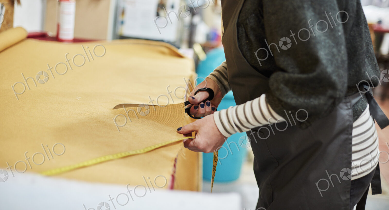A woman cutting out yellow upholstery fabric on a workbench with a large pair of scissors.