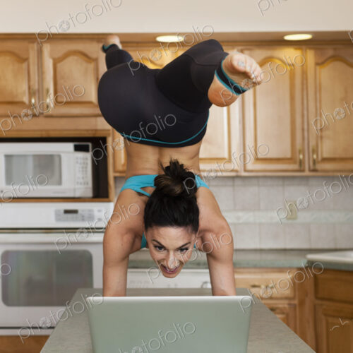 A woman doing a handstand balancing on a kitchen top and checking her laptop. A woman doing a handstand balancing on a kitchen top and checking her laptop.