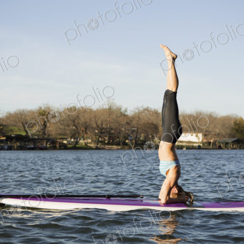 A woman doing a headstand on a paddle board on lake A woman doing a headstand on a paddle board on lake