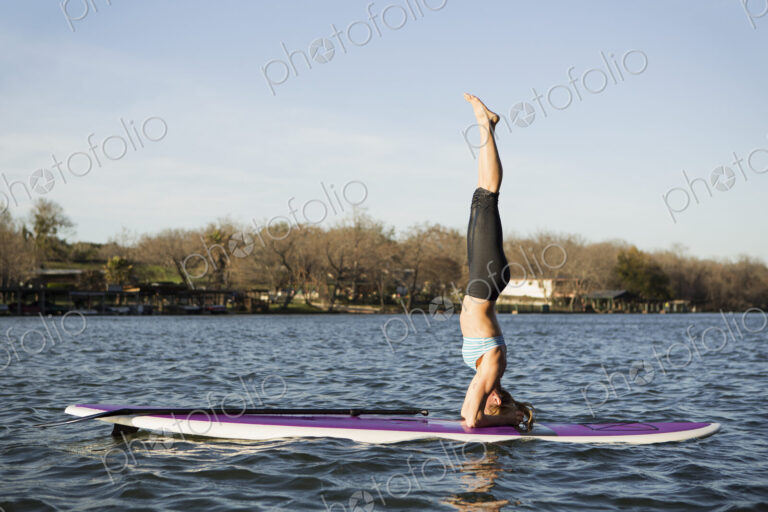 A woman doing a headstand on a paddle board on lake