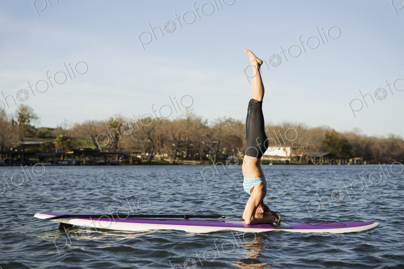 A woman doing a headstand on a paddle board on lake