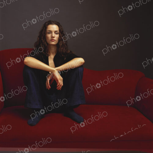 A woman dressed in black seated on a red couch. A woman dressed in black seated on a red couch.