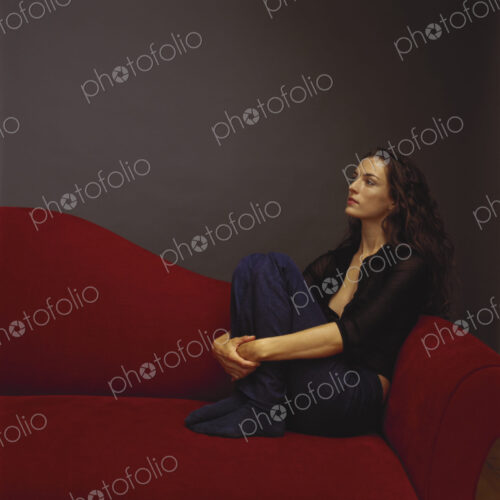 A woman dressed in black seated on a red couch. A woman dressed in black seated on a red couch.