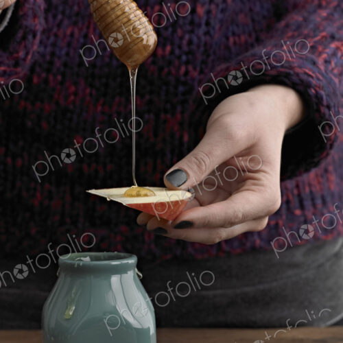 A woman drizzling honey from a round wooden drizzle stick on to an apple slice. A woman drizzling honey from a round wooden drizzle stick on to an apple slice.