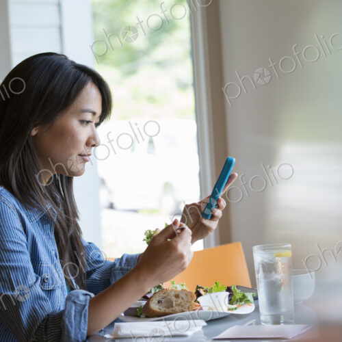 A woman eating a salad, and checking her phone. A woman eating a salad, and checking her phone.