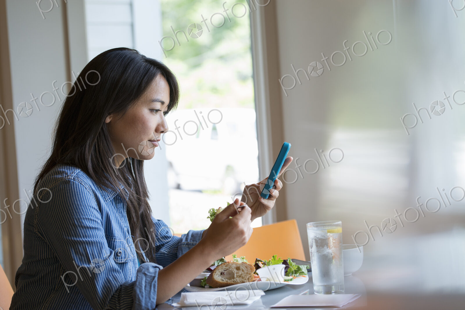 A woman eating a salad, and checking her phone.