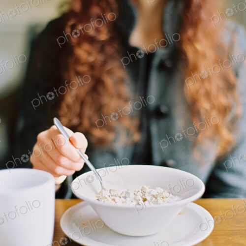 A woman eating breakfast cereal from a white bowl.