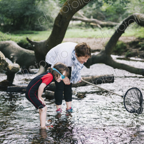 A woman giving a boy a piggyback and holding a shrimping net wading in a shallow stream. A woman giving a boy a piggyback and holding a shrimping net wading in a shallow stream.