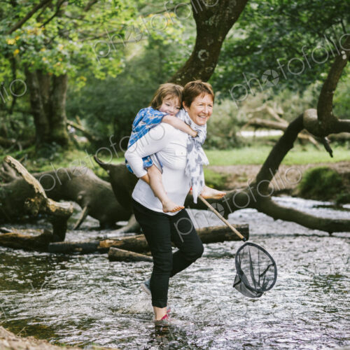 A woman giving a boy a piggyback and holding a shrimping net wading in a shallow stream. A woman giving a boy a piggyback and holding a shrimping net wading in a shallow stream.