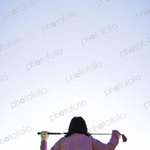 A woman golfer holding a club over her shoulders.