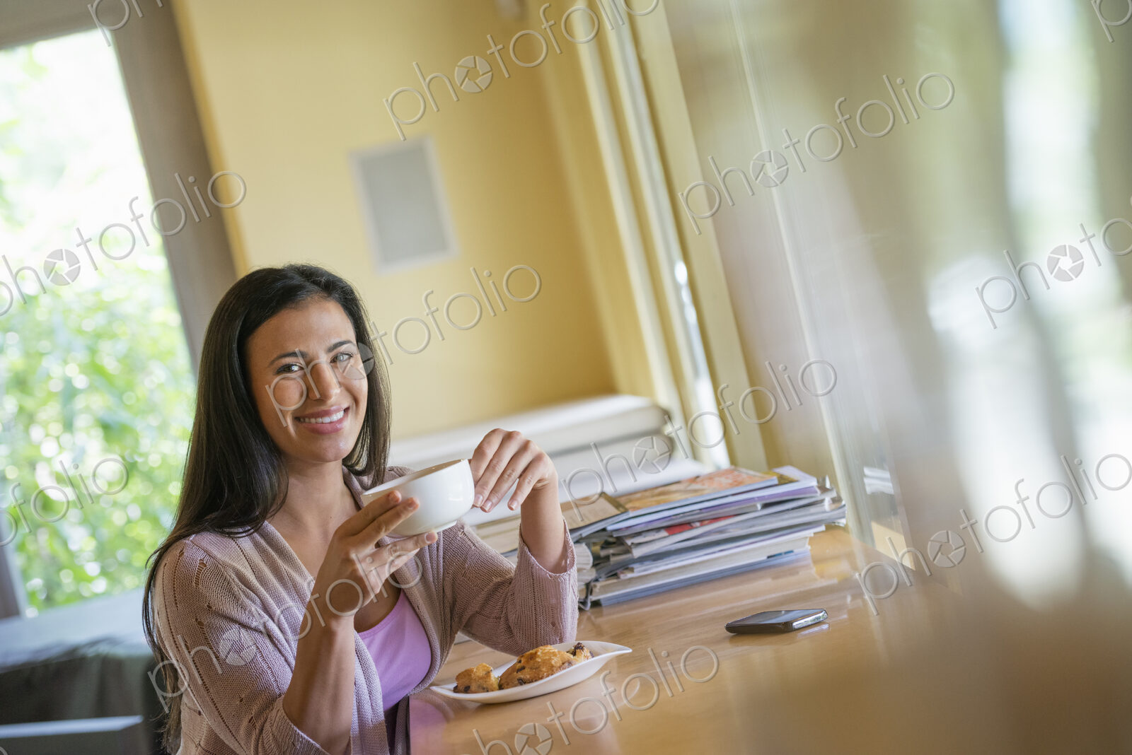 A woman having a cup of coffee. A smart phone lying on the table.