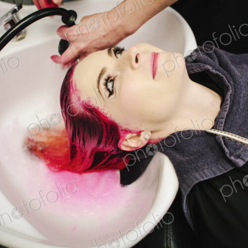 A woman having her hair rinsed with red dye running into the basin.
