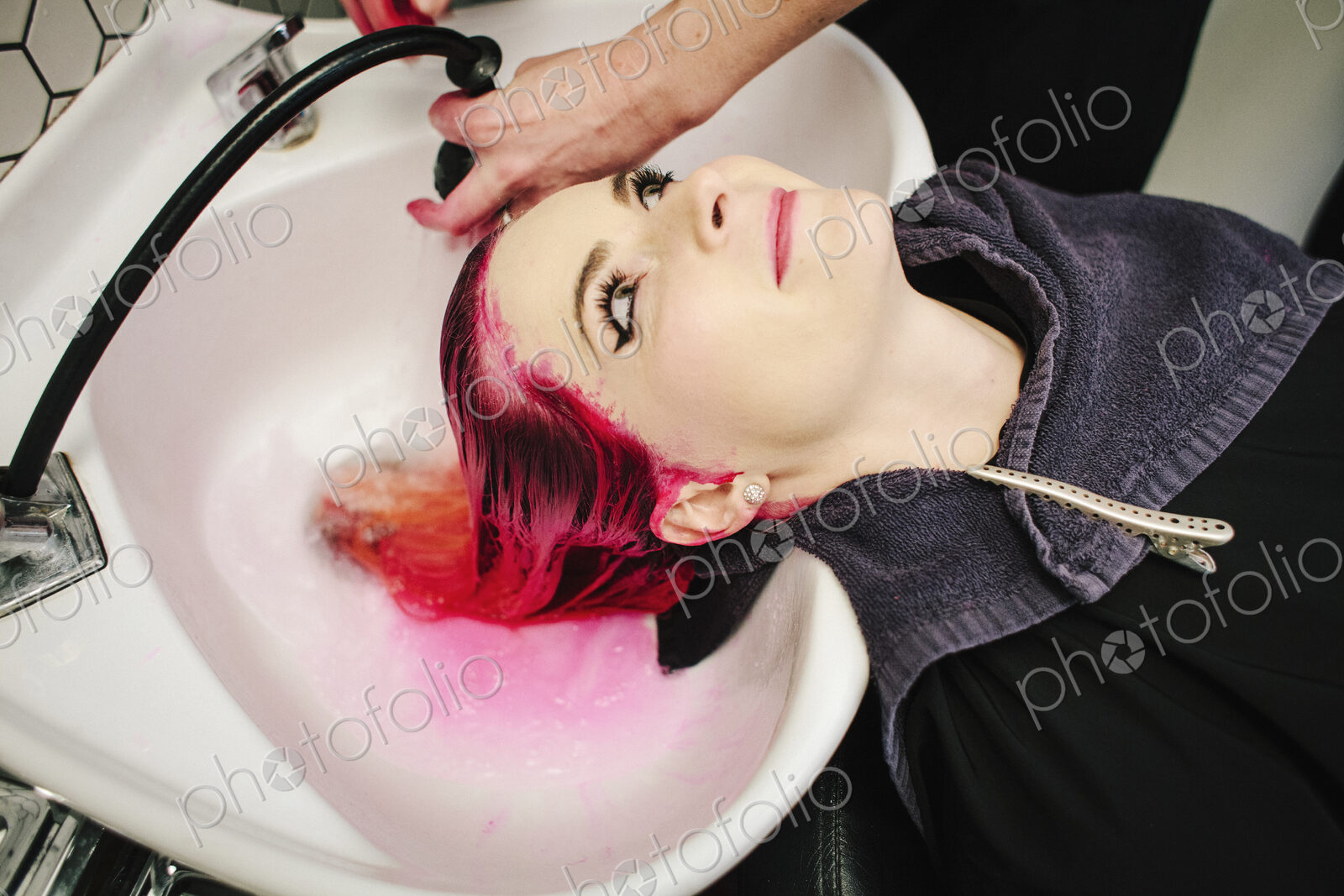A woman having her hair rinsed with red dye running into the basin.