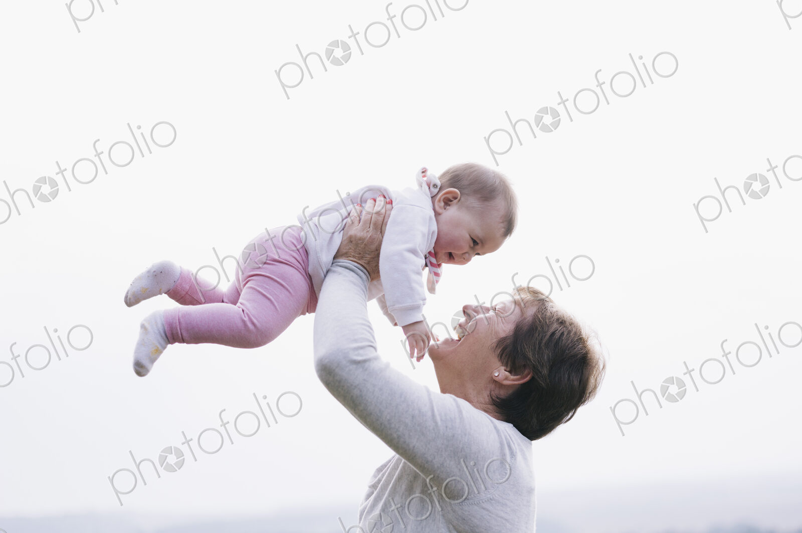 A woman holding a baby girl in the air above her head.