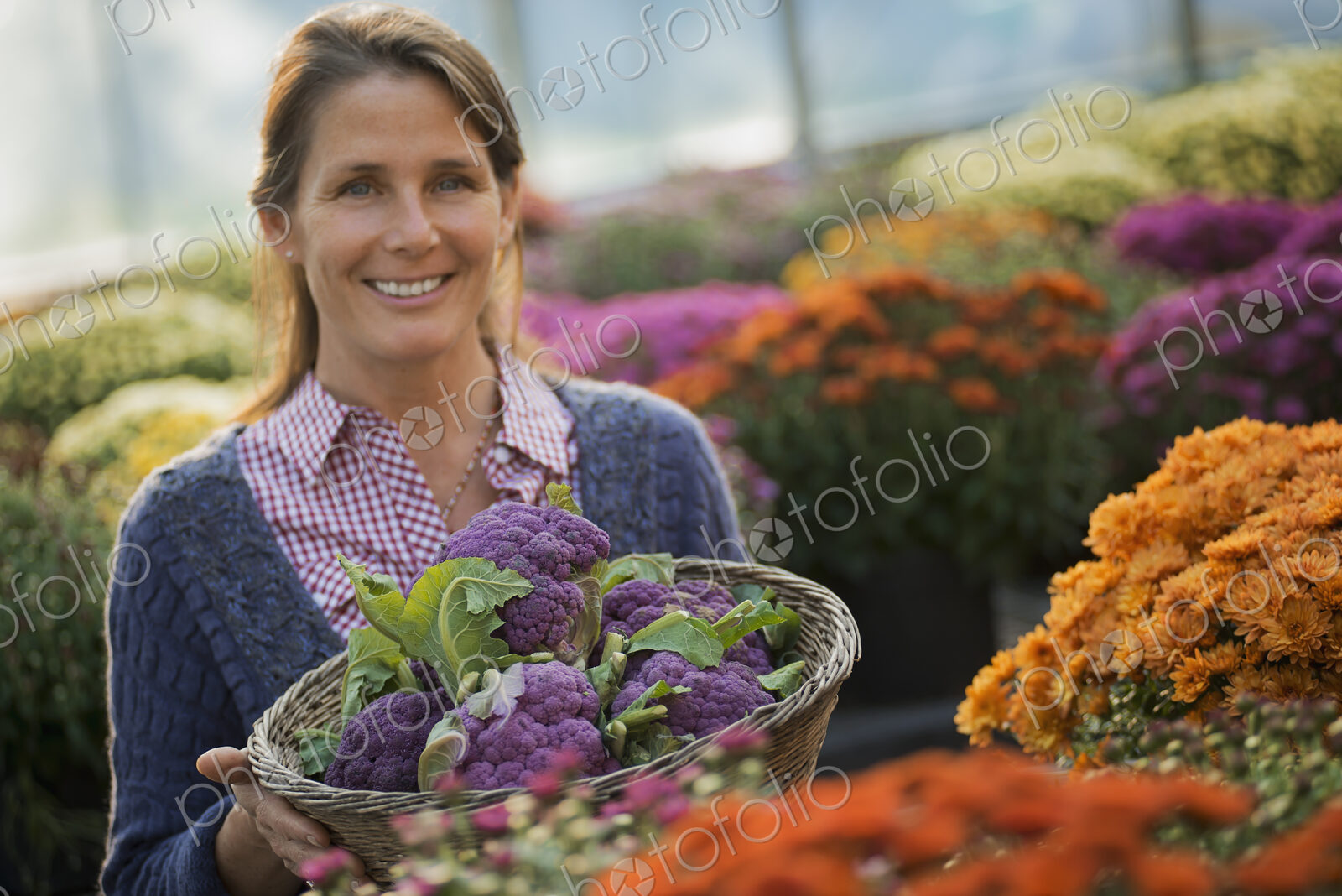 A woman holding a bowl of fresh produce, purple sprouting broccoli. Flowering plants.…