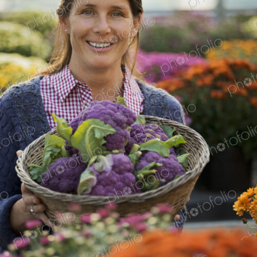 A woman holding a bowl of fresh produce, purple sprouting broccoli. Flowering plants.…