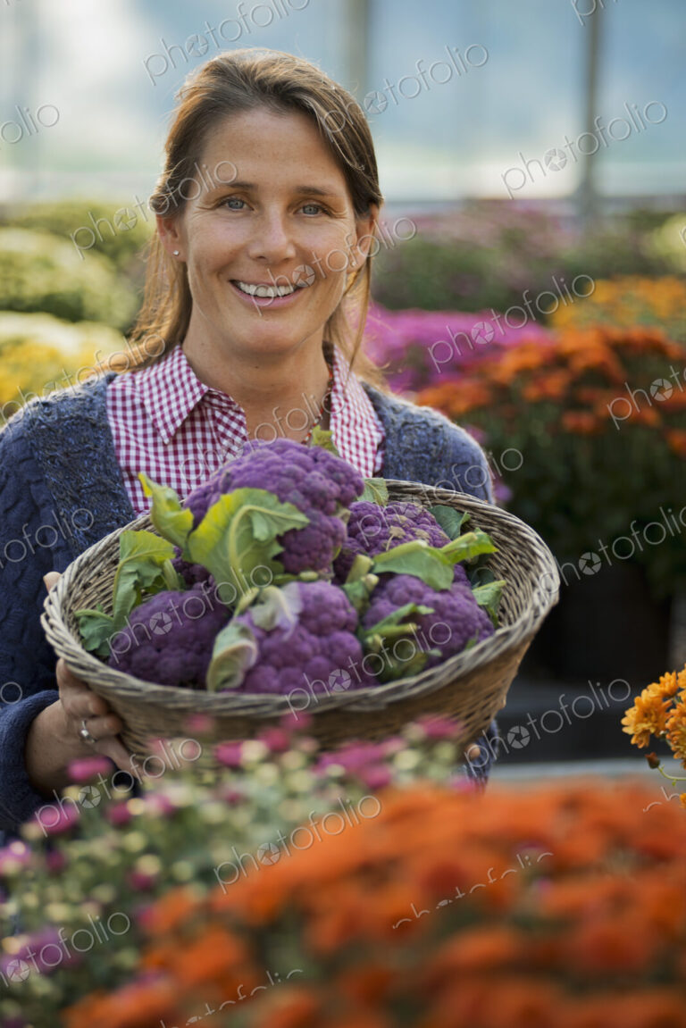 A woman holding a bowl of fresh produce, purple sprouting broccoli. Flowering plants.…