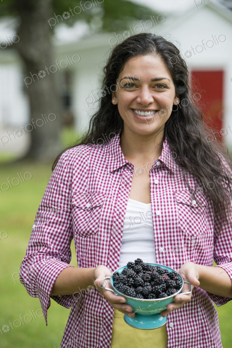 A woman holding a bowl of freshly picked blackberries.