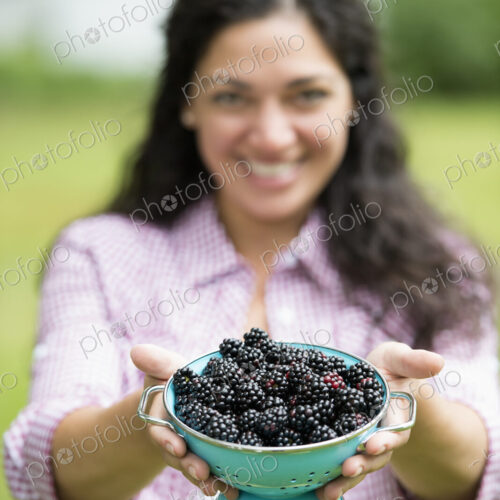 A woman holding a bowl of freshly picked blackberries.