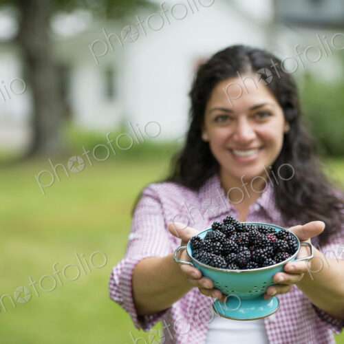 A woman holding a bowl of freshly picked blackberries.