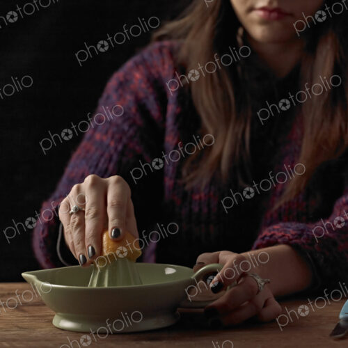 A woman holding a cut orange half, and using an orange squeezer to extract the juice,…