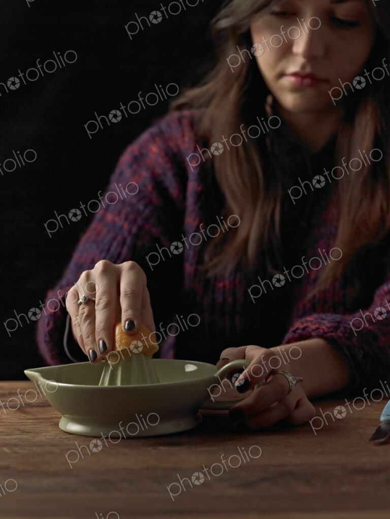 A woman holding a cut orange half, and using an orange squeezer to extract the juice,…