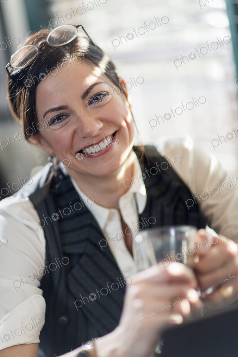 A woman holding a glass and smiling at the camera. A working lunch.