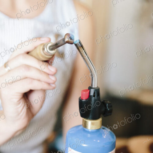 A woman holding a hand tool to the flame of a blow torch, heating metal.