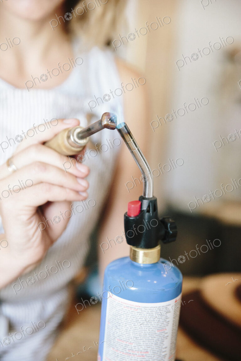 A woman holding a hand tool to the flame of a blow torch, heating metal.