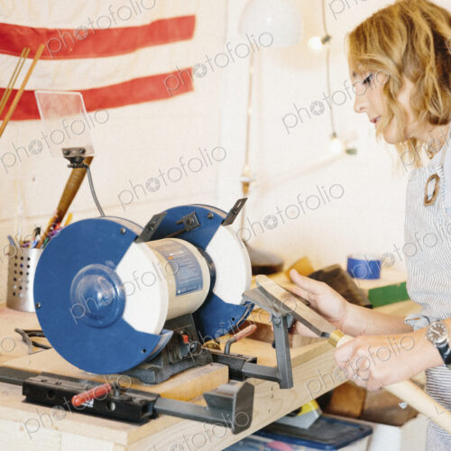 A woman holding a knife shaped steel with a long handle on a rotary grinder.