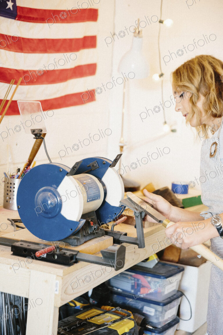 A woman holding a knife shaped steel with a long handle on a rotary grinder.