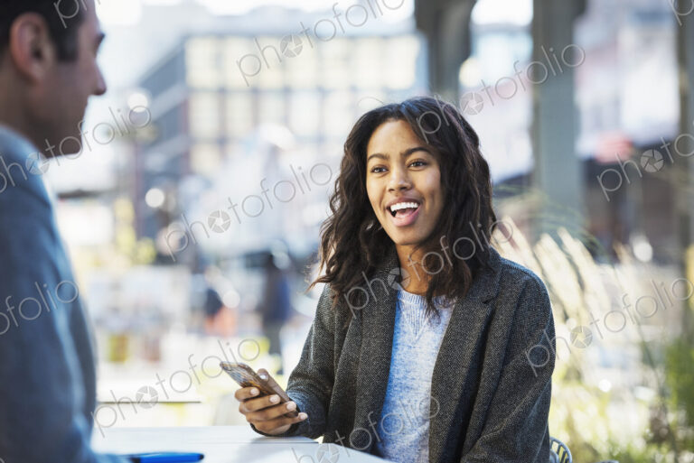 A woman holding a mobile phone, talking to a man on a city street.