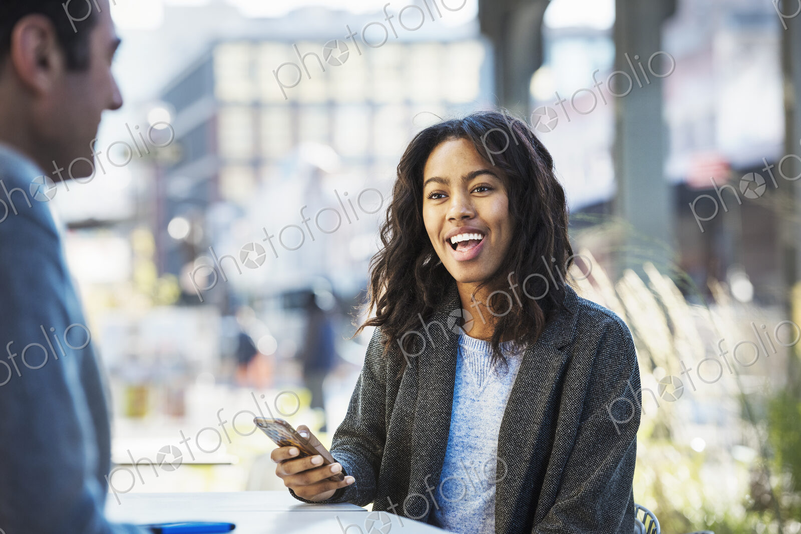 A woman holding a mobile phone, talking to a man on a city street.
