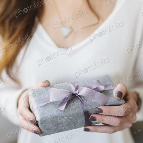 A woman holding a package with a large ribbon wrapped around it. A woman holding a package with a large ribbon wrapped around it.