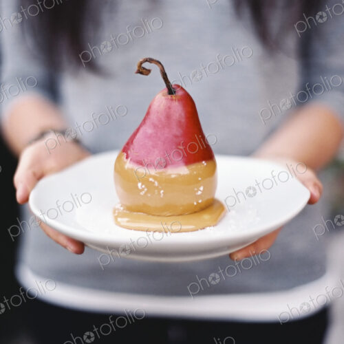 A woman holding a plate with a dessert of fresh organic pear dipped in fudge sauce. A woman holding a plate with a dessert of fresh organic pear dipped in fudge sauce.