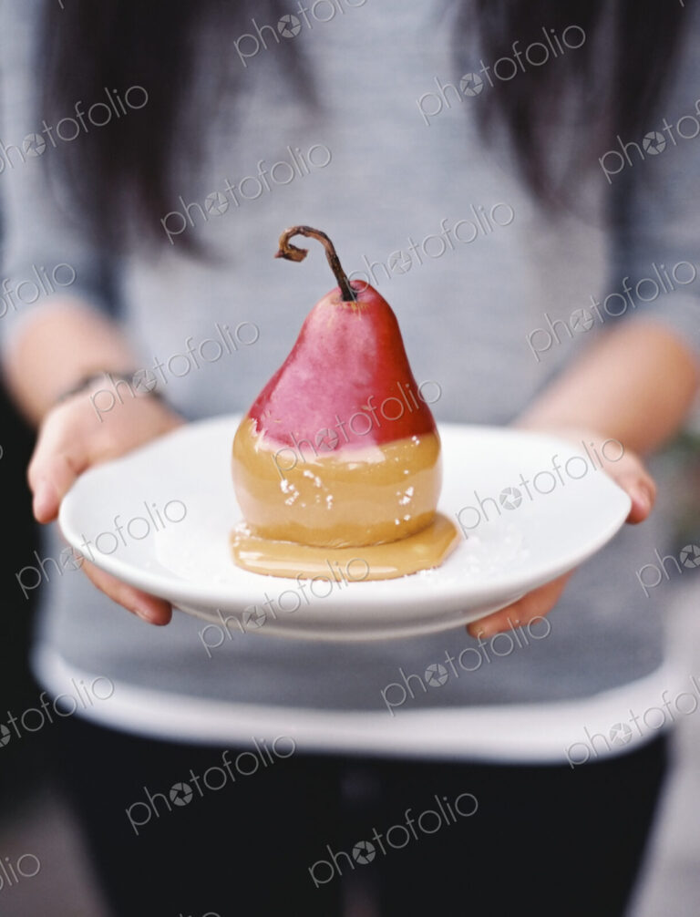 A woman holding a plate with a dessert of fresh organic pear dipped in fudge sauce.