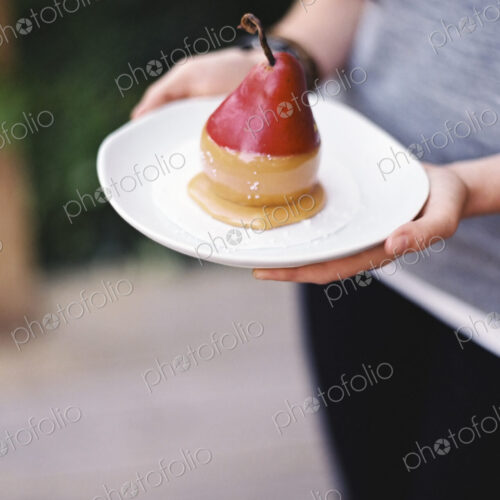 A woman holding a plate with a dessert of fresh organic pear dipped in fudge sauce. A woman holding a plate with a dessert of fresh organic pear dipped in fudge sauce.