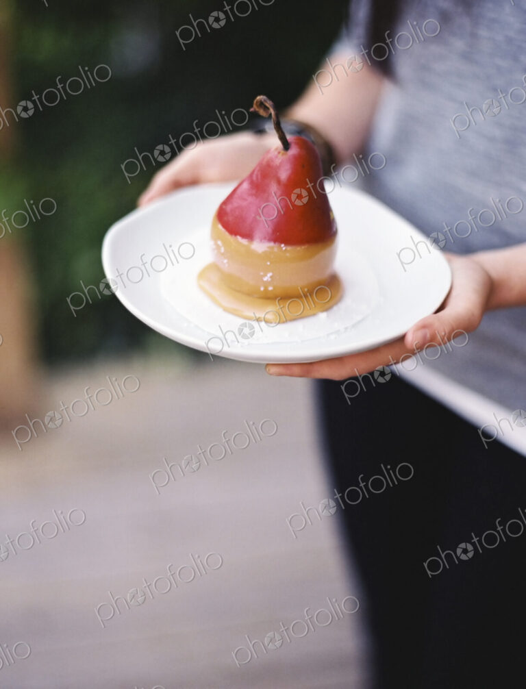 A woman holding a plate with a dessert of fresh organic pear dipped in fudge sauce.