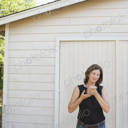 A woman holding a small fluffy chick, a baby bird in her two hands.