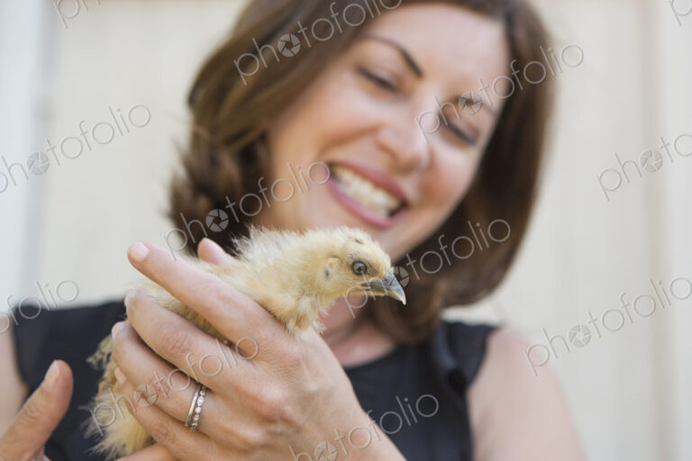 A woman holding a small fluffy chick, a baby bird in her two hands.