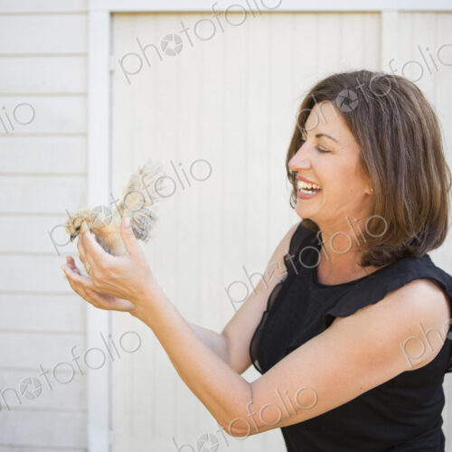 A woman holding a small fluffy chick, a baby bird in her two hands.