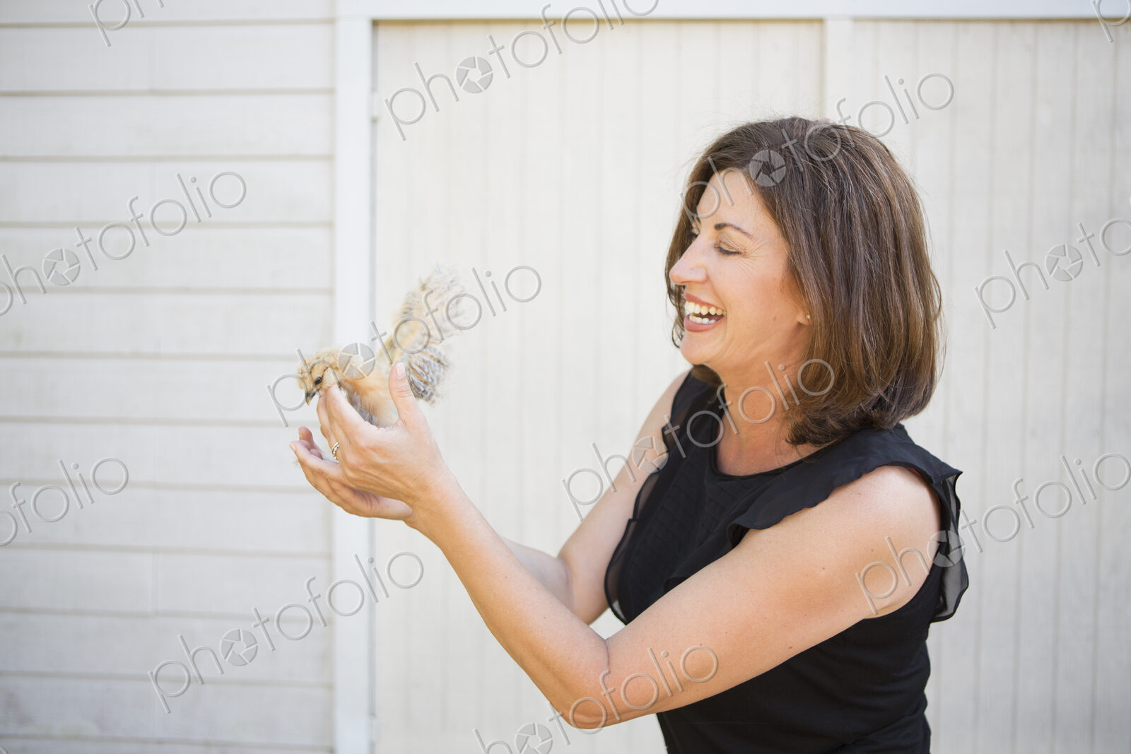A woman holding a small fluffy chick, a baby bird in her two hands.