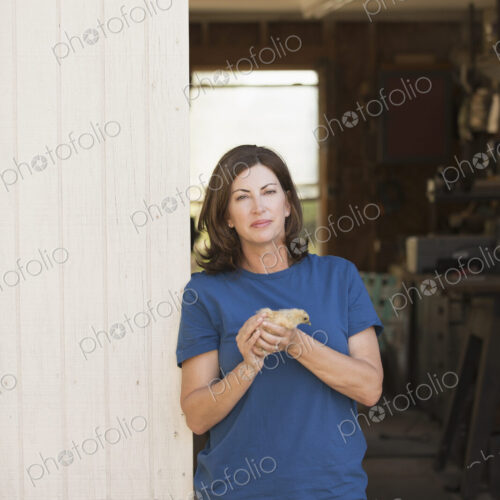 A woman holding a small fluffy chick, a baby bird in her two hands, standing at an…