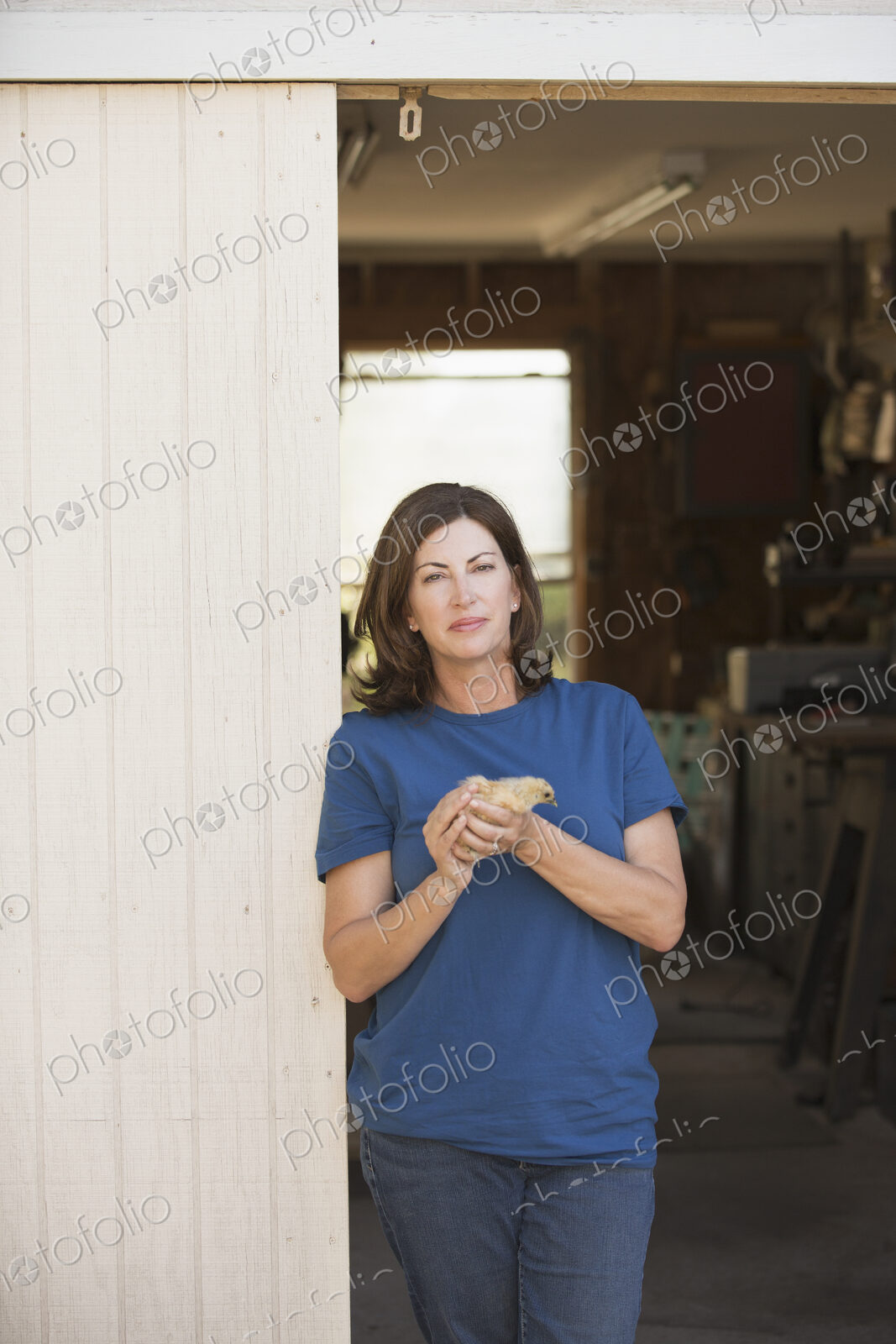 A woman holding a small fluffy chick, a baby bird in her two hands, standing at an…