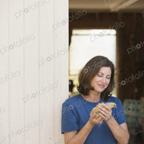A woman holding a small fluffy chick, a baby bird in her two hands, standing at an…