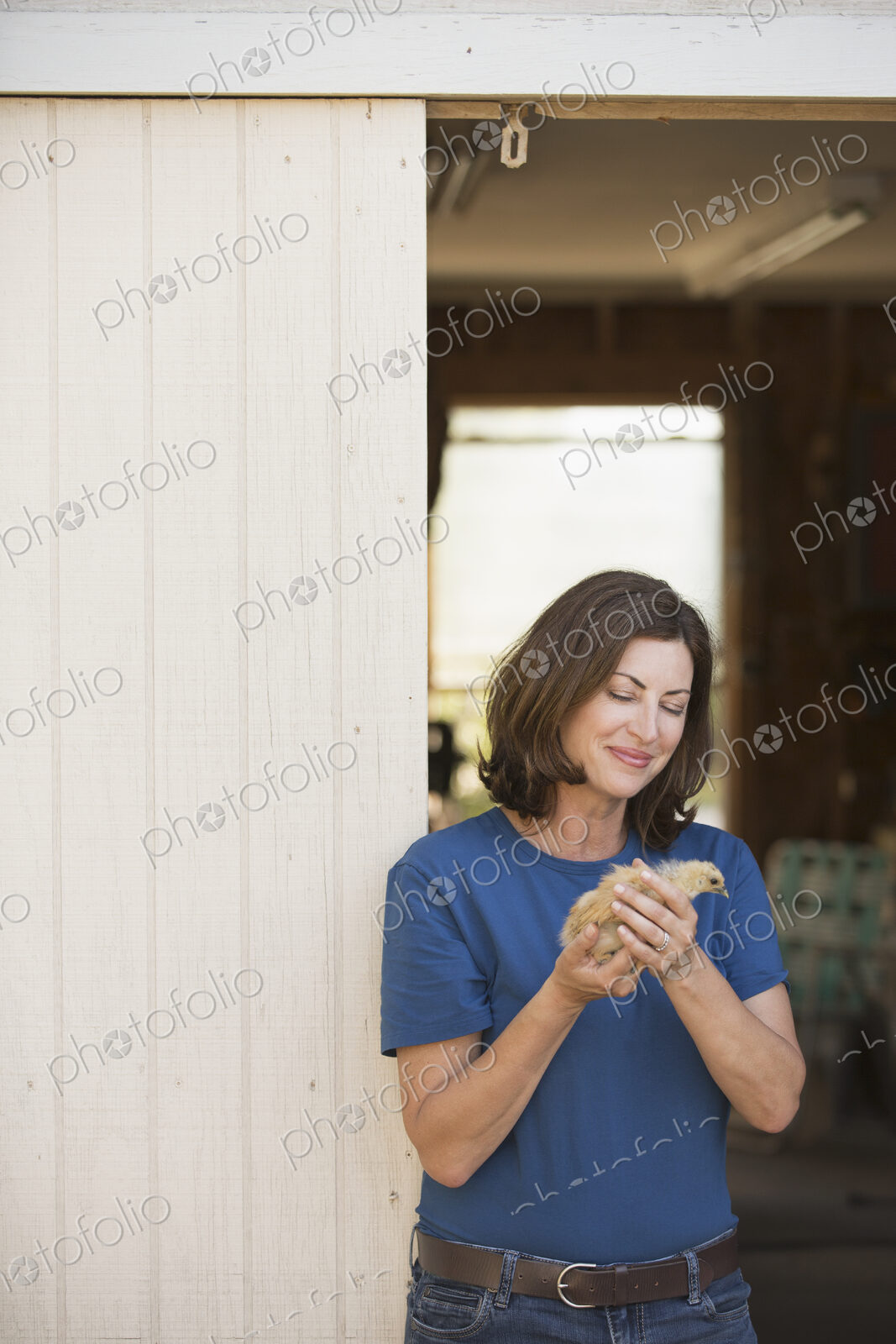 A woman holding a small fluffy chick, a baby bird in her two hands, standing at an…