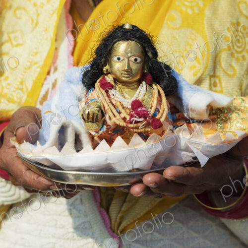 A woman holding a small puja offering, a shell shape with a small diety figure, a… A woman holding a small puja offering, a shell shape with a small diety figure, a…