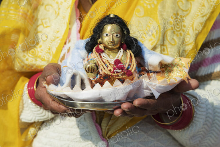 A woman holding a small puja offering, a shell shape with a small diety figure, a…