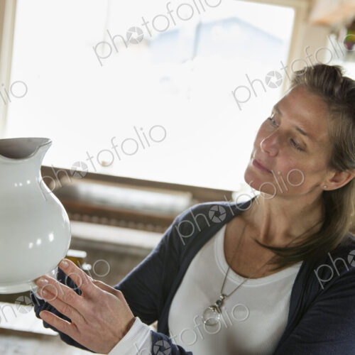 A woman holding a white pottery jug in an antique goods and furniture store. A woman holding a white pottery jug in an antique goods and furniture store.