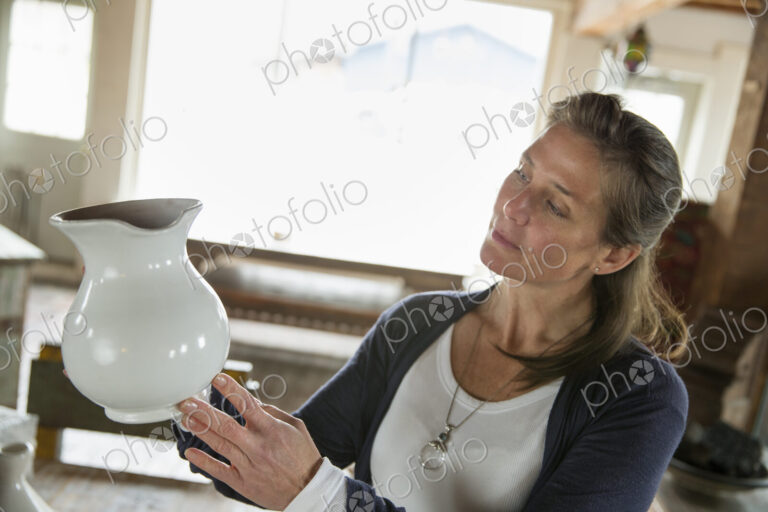 A woman holding a white pottery jug in an antique goods and furniture store.